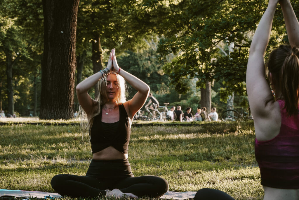 women performing yoga in park with namaste pose